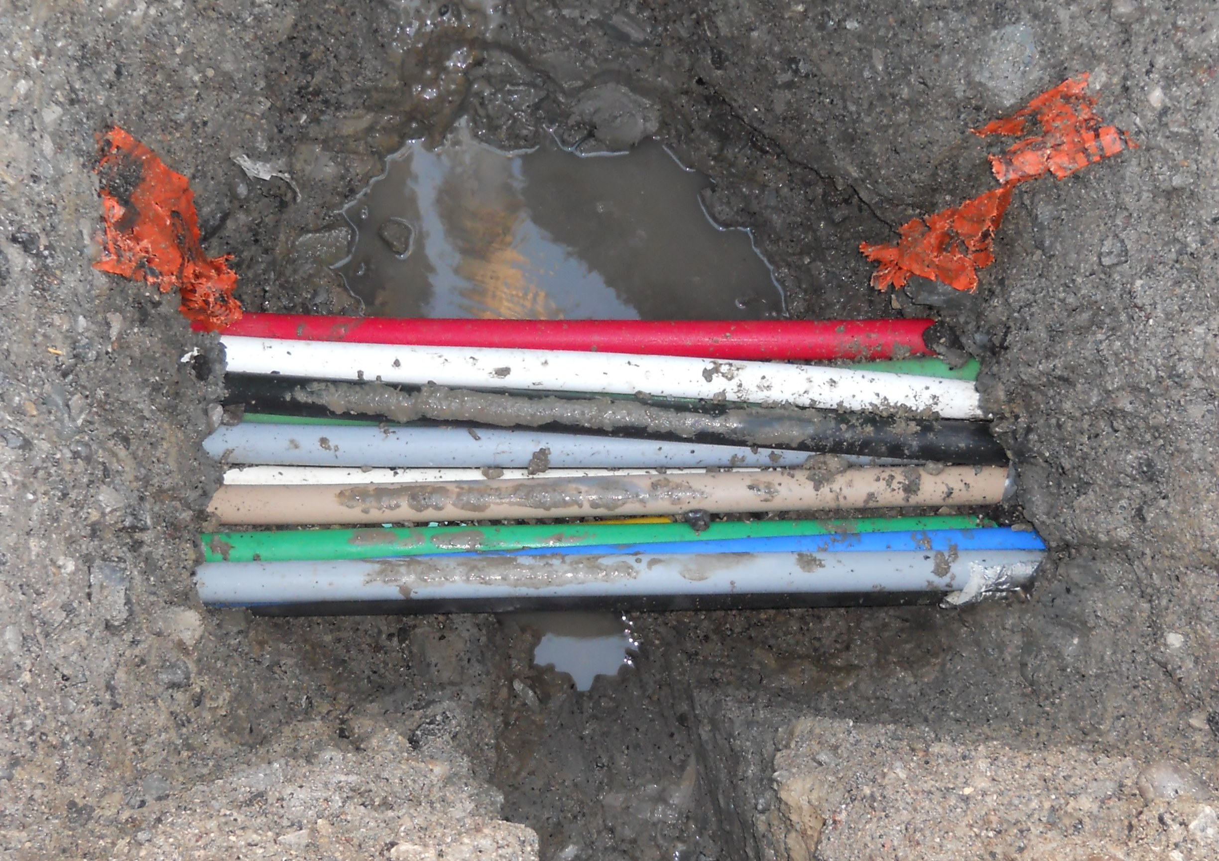 Informative Image showing a group of utilities (pipes and conduit) that have been exposed as a result of Hydro Vacuum Excavation performed by multiVIEW field technicians on a major roadway. Several utility pipes and conduits can be seen group together in parallel.