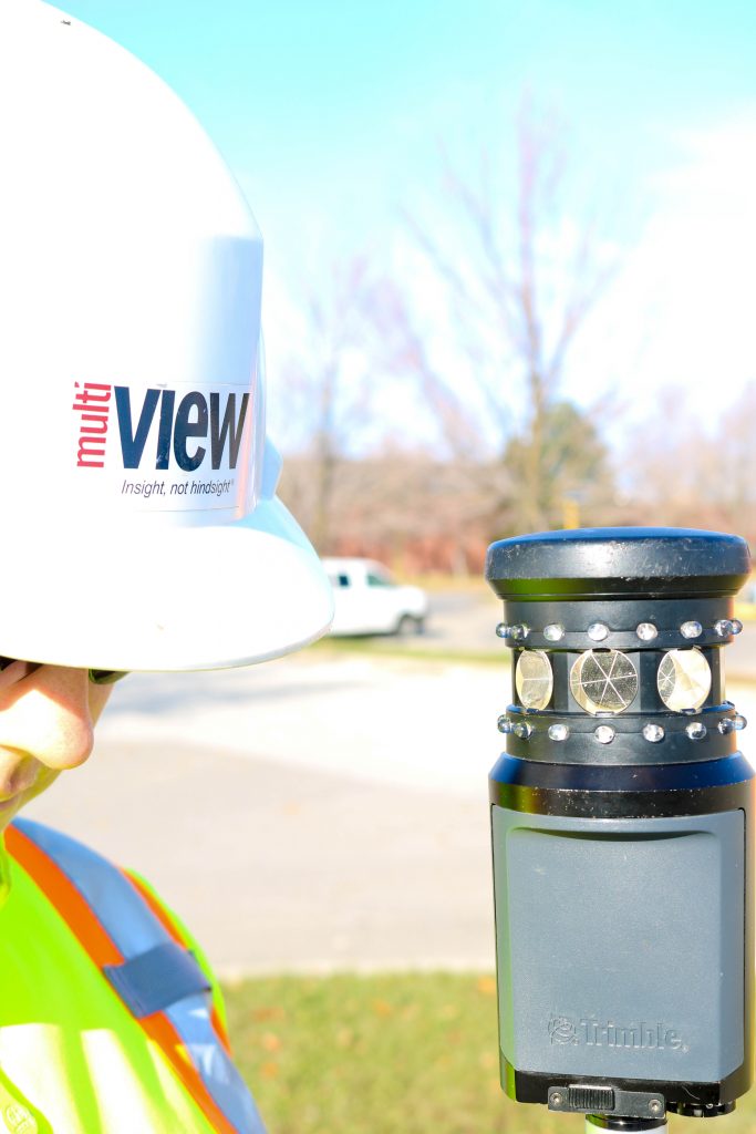 Informative Image shows a close-up of a field technician wearing a multiVIEW hardhat and standing next to GNNS hardware unit, taking accurate data on buried utilities of surveyor’s project area.