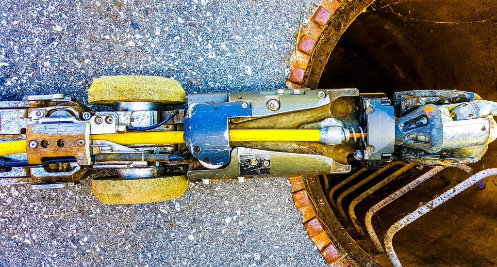 Informative Image showing a top-down, close up view of a multiVIEW rugged robotic and push Closed Circuit Television (CCTV) sewer camera system situated at the mouth of an open sewer manhole.