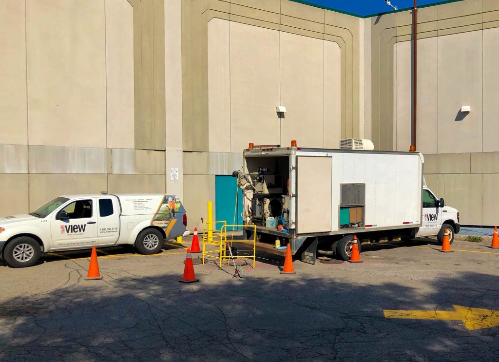 Informative Image of multiVIEW CCTV Sewer Inspection equipment truck stationed in a mall parking lot performing a wastewater infrastructure video inspection using sewer manhole as equipment entry site. Orange traffic pylons have been strategically placed around the truck and project area to ensure the safety of field technicians, equipment, and general public.